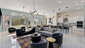 A modern living room with a sofa, chairs, and a coffee table. There is a kitchen area with white cabinets and a dining area with a table and chairs.