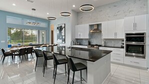 A modern kitchen with a central island, bar stools, stainless steel appliances, and a view of the outdoors.