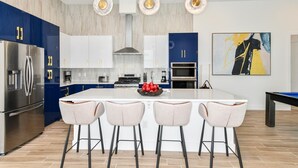 Une cuisine moderne dotée d’un îlot central, d’appareils électroménagers en acier inoxydable et de tabourets de bar.
