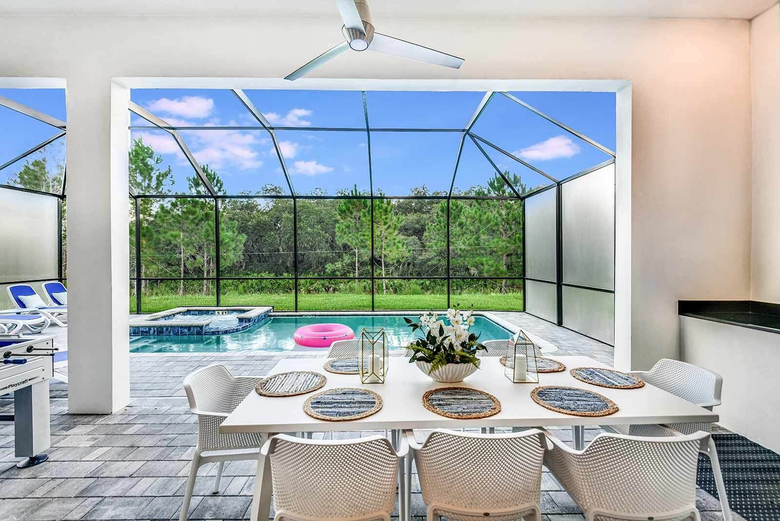 A modern outdoor dining area with a view of a swimming pool and lush greenery.