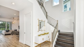 Un intérieur moderne avec un escalier, une console blanche agrémentée de détails dorés et une grande fenêtre donnant sur un jardin.