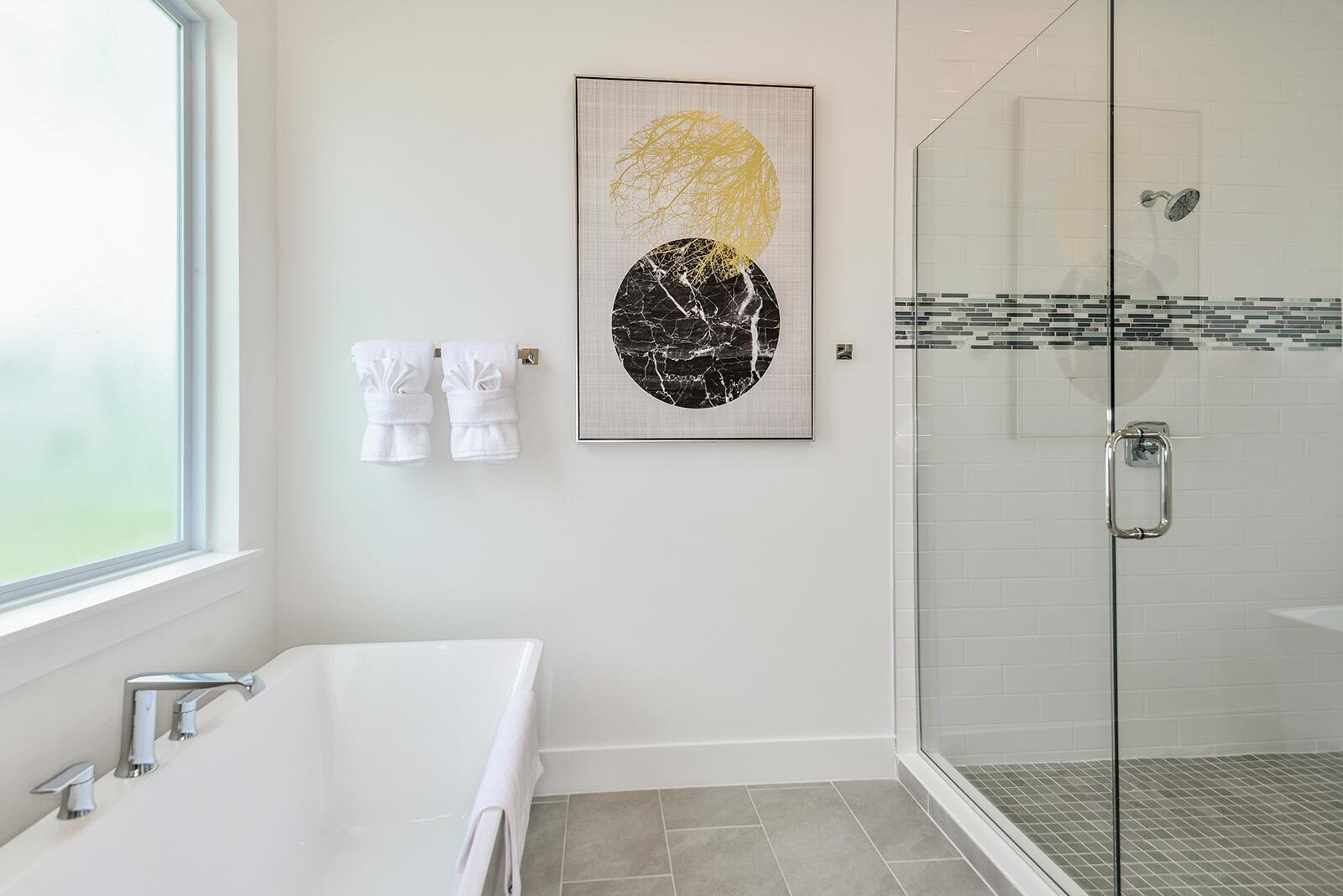 A modern bathroom with a glass-enclosed shower, a white bathtub, and a framed artwork on the wall.