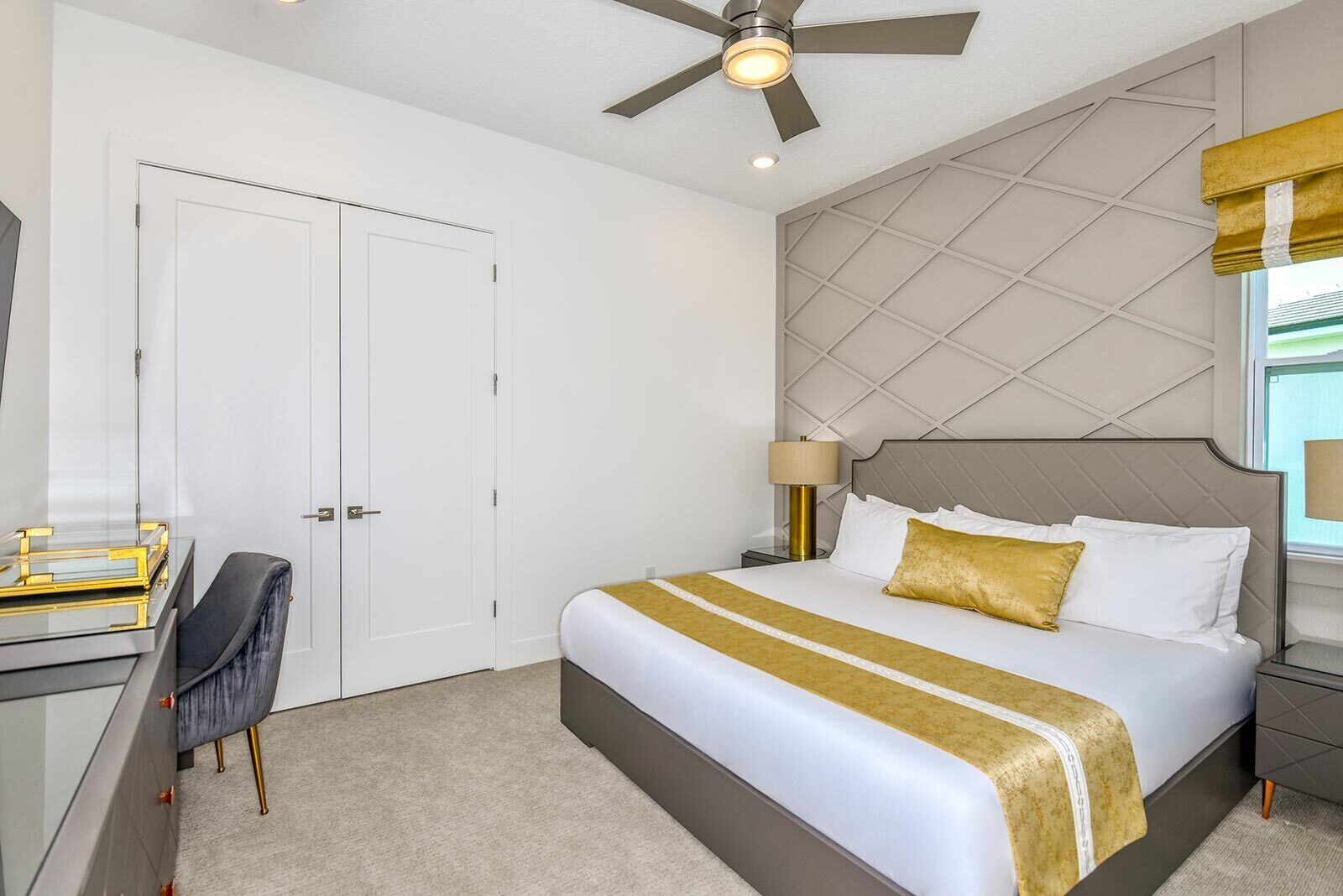 A hotel room with a bed, a desk, a chair, a ceiling fan, and a window with a view.