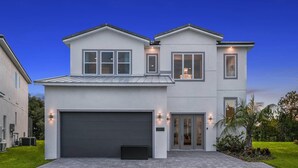 Une maison moderne à deux étages, dotée d’un garage, de grandes fenêtres et d’un éclairage extérieur.