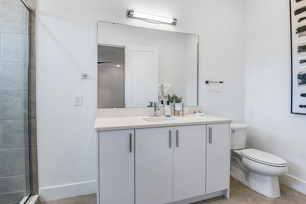 A modern bathroom with a white vanity, a large mirror, a toilet, and a shower area.