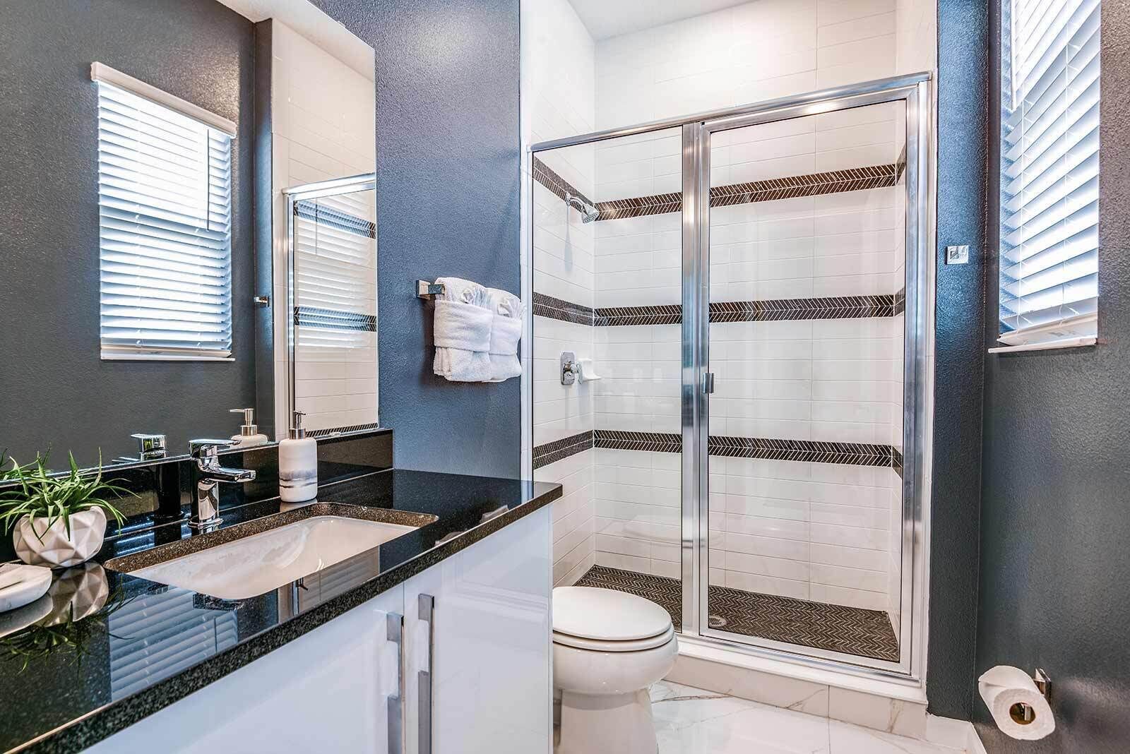 A modern bathroom with a glass shower, a black countertop, and a white toilet.
