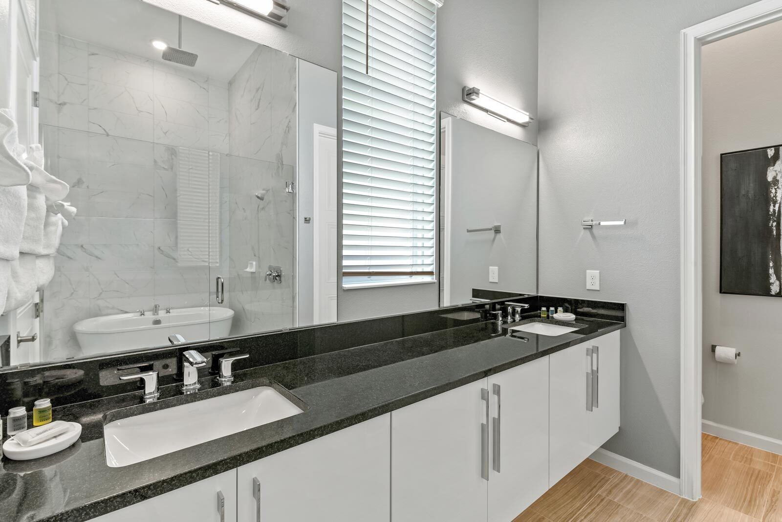 A modern bathroom with a large mirror, two sinks, and a shower.