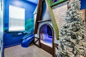 Una sala de juegos con un tobogán, un arco pequeño y un árbol decorativo.