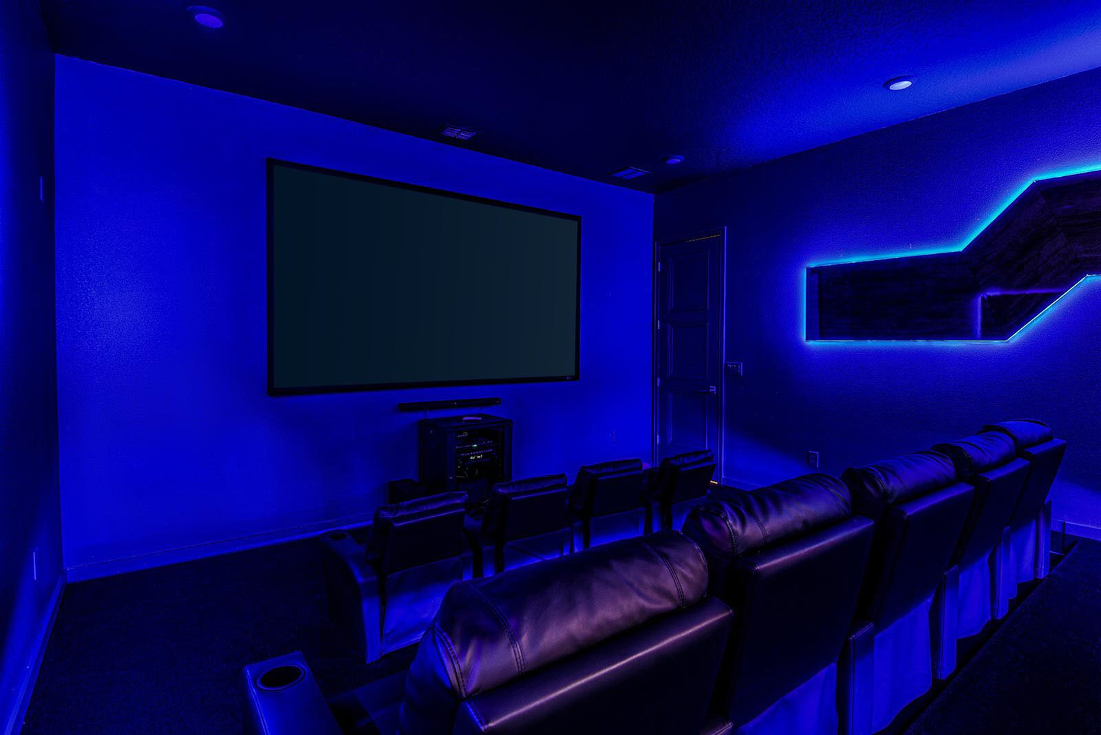 A room with a large screen, leather seating, and a staircase with blue lighting.