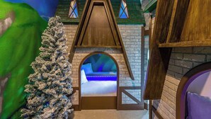 Un espace de jeux intérieur accueillant, avec une maisonnette en bois, un sapin de Noël et un toboggan.