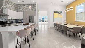 Une cuisine moderne dotée d’un îlot central, de tabourets de bar et d’un coin repas avec une longue table et des chaises.