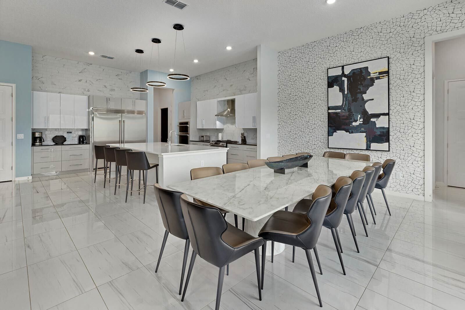 A modern kitchen with white cabinets, a marble island, and a dining area with a large table and chairs.