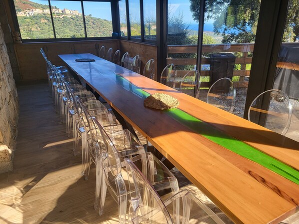 A long wooden table with clear chairs, a woven placemat, and a view of a hillside through large windows.