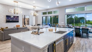 A spacious kitchen with a large island, modern pendant lights, and a view of a basketball court through large windows.