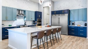 A modern kitchen with a central island, blue cabinets, stainless steel appliances, and pendant lighting.