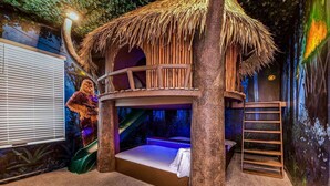 A treehouse bedroom with a thatched roof, bunk beds, and a slide.