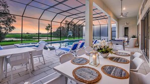 A covered outdoor area with a pool, lounge chairs, and a table set for dining.