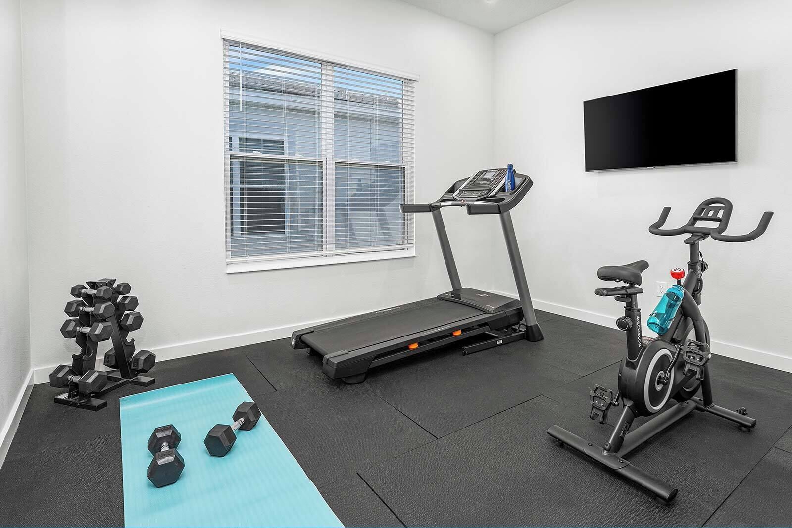 Une salle de sport équipée d’un tapis de course, d’un vélo d’appartement, d’haltères et d’un tapis bleu.