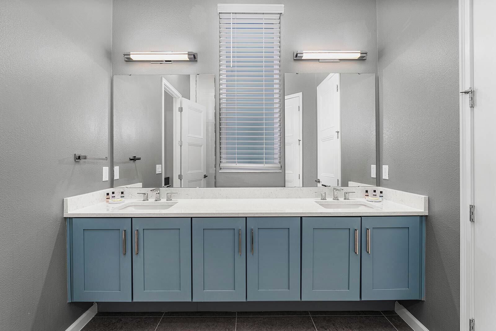 Een badkamer met een dubbele wastafel, twee wasbakken, een grote spiegel en een raam met blinds.