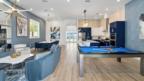 A modern living room with a pool table, a dining area, and a kitchen.