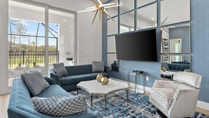 A modern living room with a sectional sofa, a patterned armchair, a coffee table, and a flat-screen TV mounted on the wall.