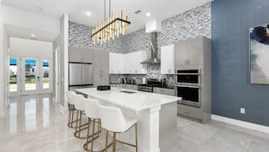 A modern kitchen with a large island, stainless steel appliances, and a unique backsplash. - Stylish Home Near Disney w/ Secret Gaming RM, Pirate BR, Theater & Pool Table (Davenport)