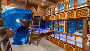 A children's play area with a blue slide and a ladder leading to a bunk bed with a view of the sky through windows. - Stylish Home Near Disney w/ Secret Gaming RM, Pirate BR, Theater & Pool Table (Davenport)