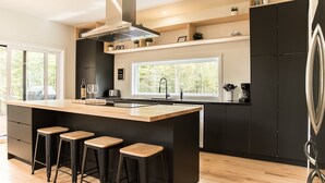 Een moderne keuken met een centraal eiland, barstoelen, zwarte keukenkastjes en een groot raam met uitzicht op de omgeving.
