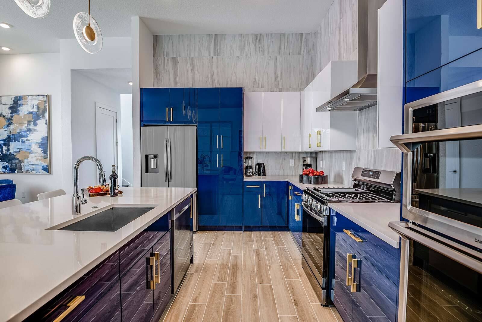 Une cuisine moderne dotée d’un îlot central, d’appareils électroménagers en acier inoxydable et de meubles de rangement bleus.
