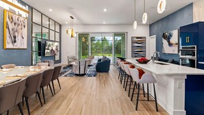 A modern kitchen with a central island, bar stools, and a dining area with a long table and chairs.