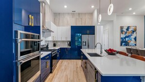 A modern kitchen with blue cabinetry, stainless steel appliances, and a large island with a sink.