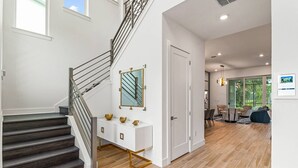 A modern interior with a staircase, a white console table with decorative bowls, a mirror, and a door leading to another room.