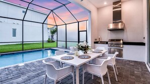 Une terrasse extérieure avec une piscine, une table à manger avec des chaises et un coin cuisine équipé d’un barbecue.