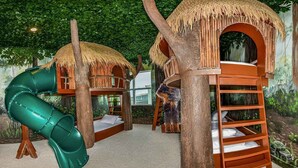 Un espace de jeux avec des structures en forme de cabane dans les arbres, un toboggan et une échelle.