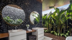 A modern bathroom with two sinks, a large mirror, and a stone wall. - Green Flow Villa 16 (Ubud)