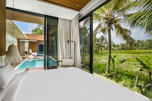 A bedroom with a large bed, a view of a swimming pool, and a lush tropical garden outside. - Green Flow Villa 16 (Ubud)