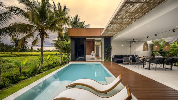 A modern pool area with lounge chairs, a wooden deck, and a view of a lush green landscape. - Green Flow Villa 16 (Ubud)
