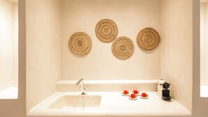 Een badkamer met een wit wastafelmeubel, drie geweven wanddecoraties en een plank met bekers en borden.