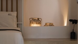 A modern bedroom with a bed, a bedside table with a vase, and a wall-mounted shelf with decorative items.