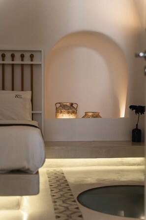 A modern bedroom with a bed, a bedside table with a vase, and a wall-mounted shelf with decorative items. - Two Bedroom Villa Outdoor Hot Tub- La Torre (Santorini)