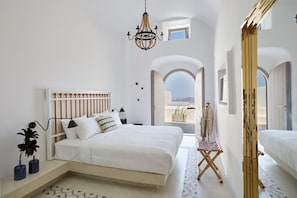 A modern bedroom with a large bed, a small table, and a view through an arched doorway.