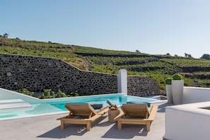 Un espace piscine agrémenté de murs en pierre, de chaises longues en bois et offrant une vue sur un paysage vallonné.