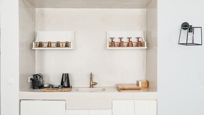 Eine kompakte Küche mit weißen Schränken, zwei Regalen mit Dekoration, einer Kaffeemaschine und einem kleinen Spülbecken.