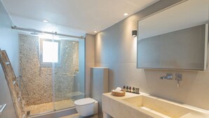 Un baño moderno con ducha de vidrio, un espejo grande y tocador con lavamanos y espacio para toallas.