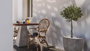 Un conjunto de sillón y mesa de mimbre frente a una pared blanca con un árbol en maceta.