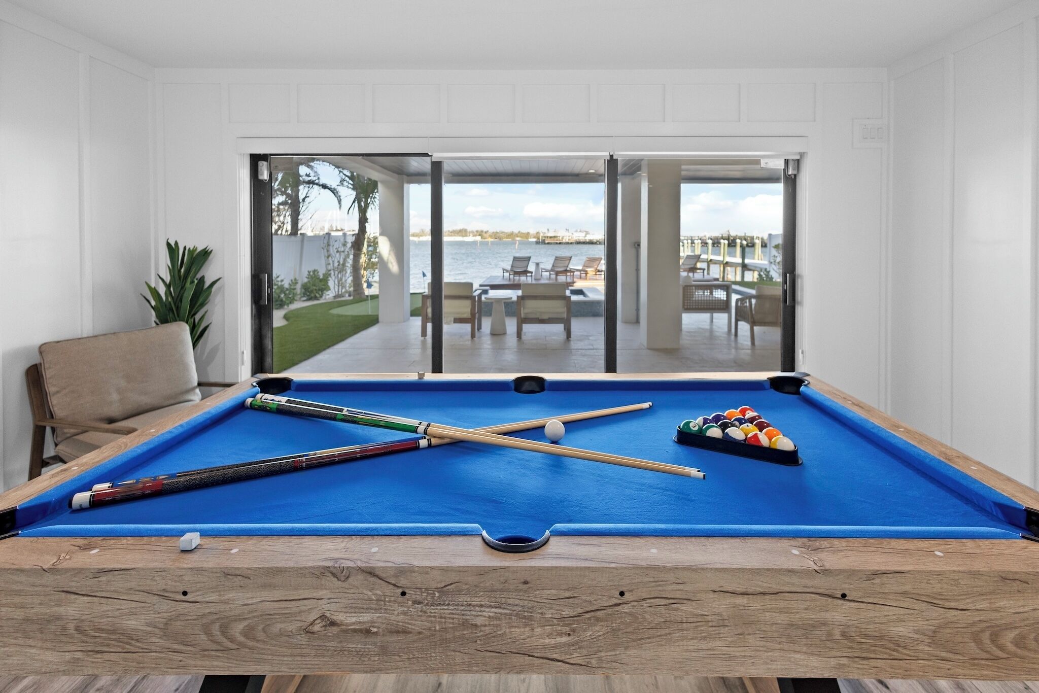 Ein Billardtisch mit Spielstöcken und Kugeln, ein Stuhl und Blick auf eine Terrasse mit Sitzgelegenheiten.
