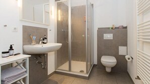Moderni kylpyhuone, jossa on lasinen suihkuseinä, valkoinen pesuallas ja wc-istuin.