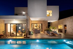 Ein modernes Haus mit Swimmingpool, Steinwänden und einem gemütlichen Innenraum mit Sitzgelegenheiten und Kamin.