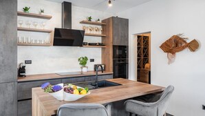A modern kitchen with a central island, bar stools, a wine rack, and a built-in oven. - Luxury Villa Praska with 3 en-suite bedrooms, Finnish Sauna, private pool (Podstrana)