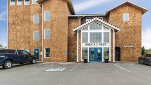 Un bâtiment à deux étages, avec une enseigne indiquant « BOLSTAD WEST » à l’entrée. Deux véhicules sont stationnés devant, et un panneau indiquant une place de stationnement réservée aux personnes handicapées est visible.
